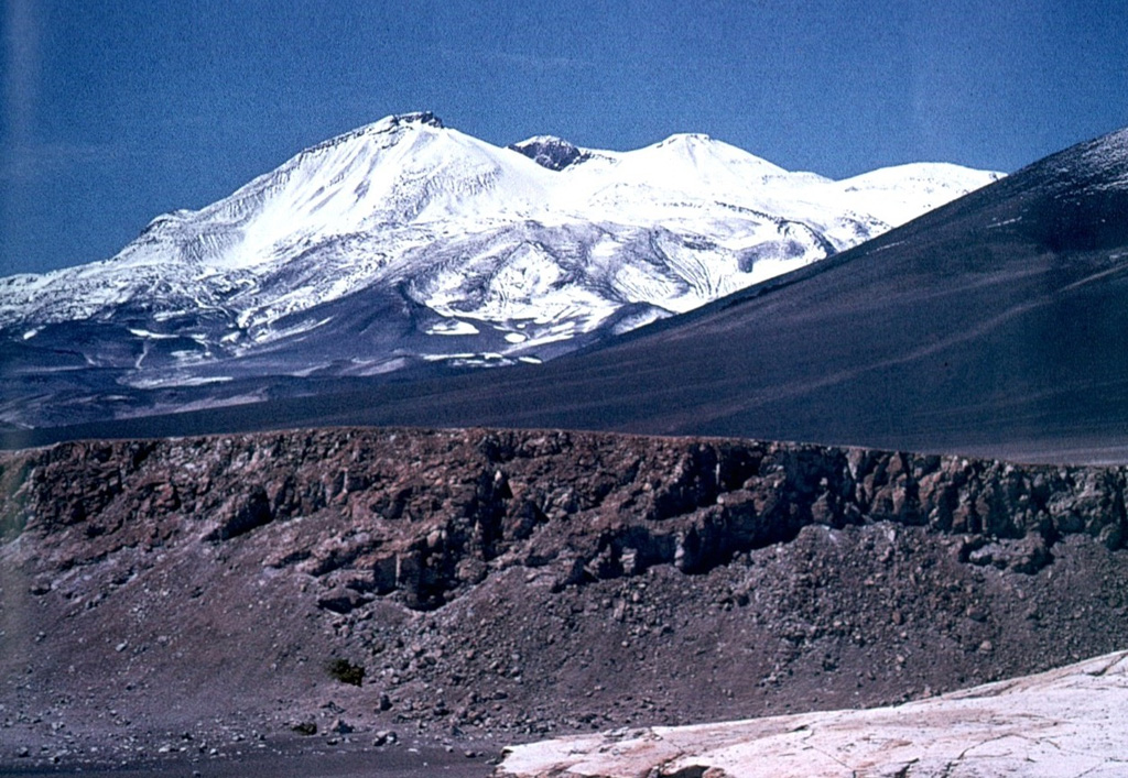 The NW side of Nevados Ojos del Salado volcano rises above Pliocene ignimbrites and pyroclastic deposits of the Barranca Blanca.  These deposits are overlain by dacitic pyroclastic-flow deposits from Ojos del Salado.  A break in slope about half way up the volcano is the rim of a somma, inside which the modern edifice was constructed.  Dacitic lava flows from the summit cone periodically overtopped the somma rim. Photo by Oscar González-Ferrán (University of Chile).
