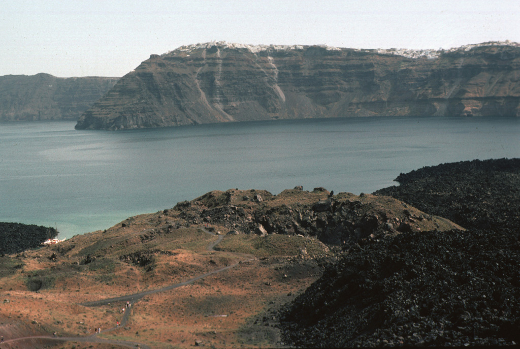 The crater in the foreground was formed during an eruption from 1570-1573 CE. Initially submarine eruptions were followed by the formation of the new island of Mikri Kameni (Little Burnt Island) NE of Palaea Kameni Island. The 1570-73 eruption created a small island with a diameter of about 400 m and a height of 70 m, topped by a 20-m-deep crater. The western wall of Santorini's caldera appears in the background, capped by the houses of the village of Merovígli. Photo by Lee Siebert, 1994 (Smithsonian Institution)