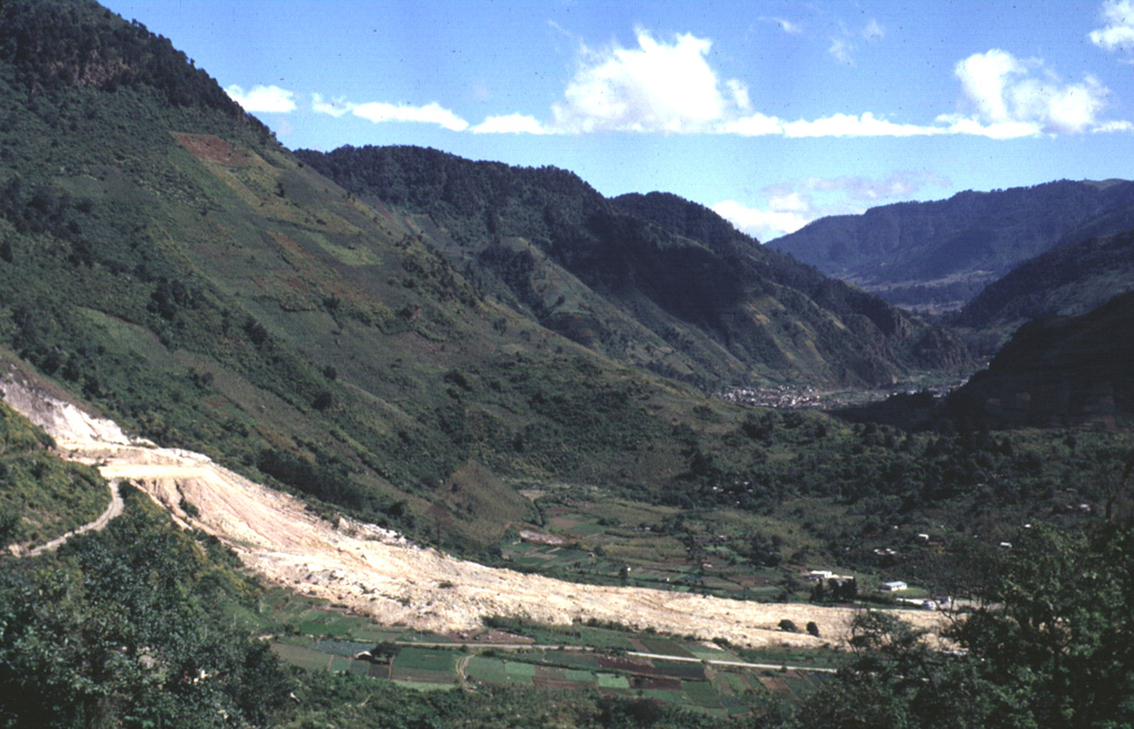 The light-colored area in the foreground is a landslide from the Almolonga volcano Zunil geothermal field that occurred on 5 January 1991. The landslide traveled 800 m from its source along the Zunil fault zone toward the Río Samalá and killed 23 people living on the valley floor and cut off the highway between Quetzaltenango and the Pacific coast. Some of the survivors of the slide were treated for burns from the hot flow. This view looks along the Río Samalá valley to the NE with the flanks of Cerro Quemado in the background to the left. Photo by Carlos Pullinger, 1993 (Servicio Nacional de Estudios Territoriales, El Salvador).