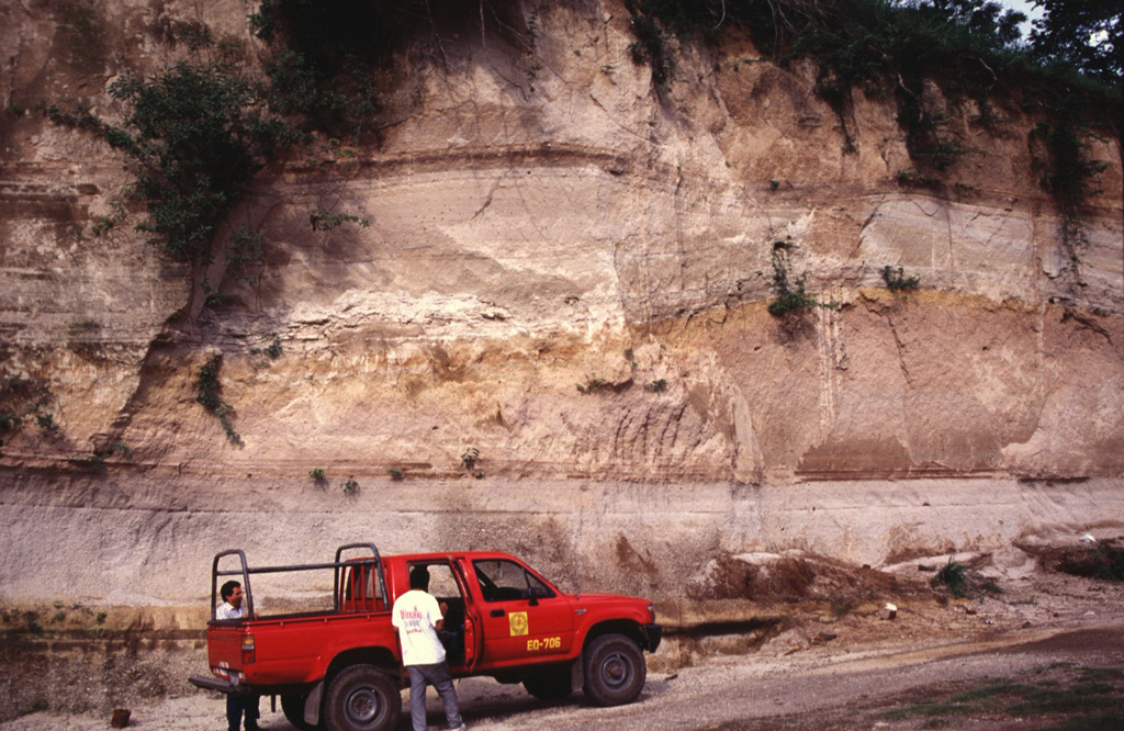 Rhyolite pumice fall and pyroclastic flow deposits from the two caldera-forming eruptions (Arce and Congo) at Coatepeque are exposed in this quarry wall. The lower Arce pumice and overlying pyroclastic flow deposit have a total volume about 40 km3 and were emplaced during the 72,000 BP eruption that formed the NE part of the caldera. The upper deposits (above the undulating brown paleosol in the center of the photo) are from the 16 km3 Congo eruption prior to about 57,000 years ago and were erupted through a caldera lake. Photo by Carlos Pullinger, 1996 (Servicio Nacional de Estudios Territoriales, El Salvador).