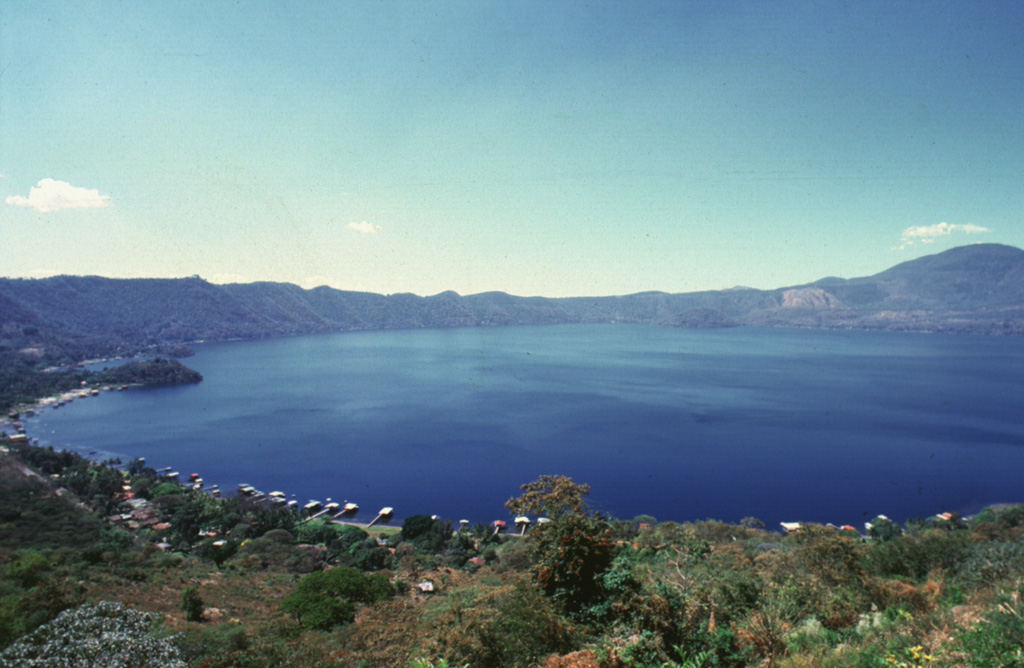 Lago de Coatepeque fills the 7 x 10 km Coatepeque caldera in western El Salvador. The caldera formed during two major eruptions in the late Pleistocene. Post-caldera eruptions produced a series of lava domes such as the one seen to the left that forms a small peninsula extending into the lake. A chain of scoria cones that erupted along caldera ring faults are across the southern caldera rim in the background. Photo by Giuseppina Kysar, 1999 (Smithsonian Institution).