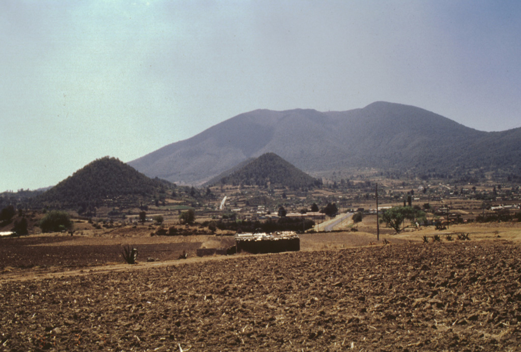 Jocotitlán rises above the Toluca basin and is seen here from the NW. This side of the edifice has a horseshoe-shaped escarpment that formed as a result of gravitational failure of the summit during the early Holocene. The conical hills of Cerro San Miguel (left) and Cerro la Cruz (center) are part of the resulting debris avalanche deposit that covers an 80 km2 area to the NE.  Photo by José Macías, 1997 (Universidad Nacional Autónoma de México).
