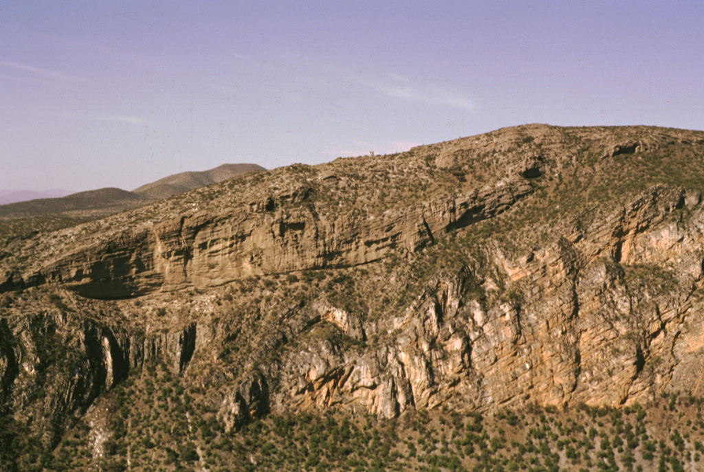 Thick deposits of folded and faulted Cretaceous limestones (lower right) are exposed in the steep 300-m-high walls of the Joya Honda maar.  The northern wall of the maar (upper left) displays up to 120 m of initially dry and then wet pyroclastic-surge deposits with dips up to 30 degrees.  The 850 x 1000 m wide maar was erupted about 1.1 million years ago. Photo by Jorge Aranda-Gómez, 1994 (Universidad Autónoma de México).