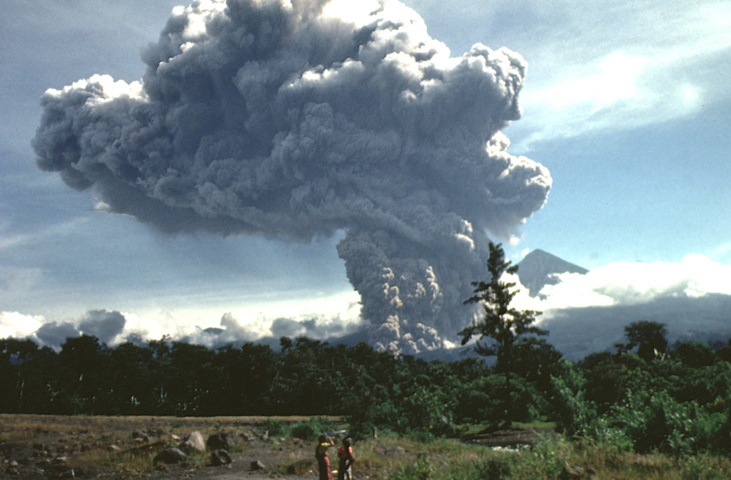 A large pyroclastic flow travels down the flank of the Santiaguito lava dome on 19 July 1989. The pyroclastic flow and ash plume are seen here from just west of El Palmar (10 km S of the dome) about 5 minutes after the start of the explosion. The Santa María summit is visible to the right of the plume, which rose to 4 km above the vent. The pyroclastic flow traveled 5 km down the Río Nimá and was one of the larger events since the major 1929-34 activity. Photo by Mike Conway, 1989 (Michigan Technological University).