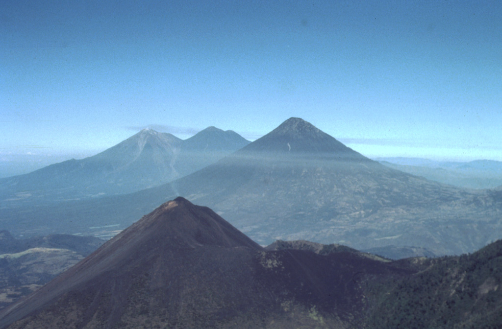This view from the east shows four major volcanoes located within 45 km of Guatemala City. In the foreground is Pacaya, which has been in frequent eruption since 1965. The modern cone (left) partially overlaps the rim of a large caldera. The large volcano in the midground horizon is Volcán de Agua. In the background is Acatenango (right) and Fuego (left).  Photo by Bill Rose, 1991 (Michigan Technological University).