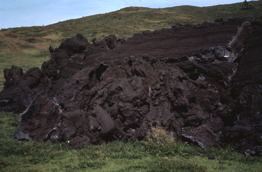 The front of the 1972 lava flow ends on grassy slopes on the southern flank of MacKenney cone at Pacaya. The rock hammer to the upper right provides scale next to the top of the flow front that formed when still-fluid lava was squeezed through an irregular crack in previously solidified crust. Photo by Bill Rose, 1972 (Michigan Technological University).