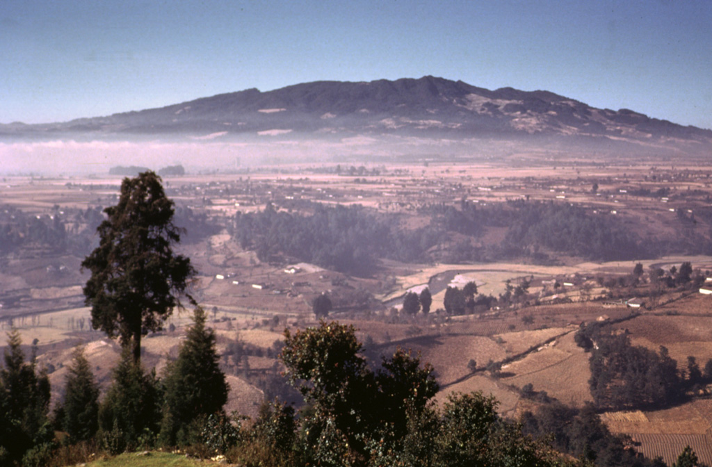 The NE flanks of the broad Siete Orejas massif rise above farmlands on the banks of the Sigüilá river.  A large caldera is breached to the south, on the opposite side of the volcano.  The volcano overlooks Quetzaltenango, Guatemala's second largest city, which is out of view to the left.  The broad irregular summit profile gives the volcano its name, which means "Seven Ears."  The latest eruption of Siete Orejas is stratigraphically constrained to have occurred between about 126,000 and 85,000 years ago.   Photo by Bill Rose, 1974 (Michigan Technological University).