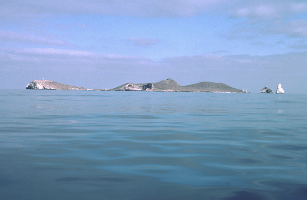 Isla Isabel, a complex of cones and associated lava flows, forms a small 1.5-km-long island located in the Pacific Ocean 30 km off the coast of Nayarit state, Mexico. The island is seen here from the SE with Cerro el Faro cone to the left and the spires of the Islotes Las Monas to the right. Isla Isabel is a wildlife sanctuary whose rocks and vegetation are mantled with white guano. Exposures of the interior of the cones forming the island can be seen in the main island sea cliffs and offshore islets. Photo by Jim Luhr, 1999 (Smithsonian Institution).