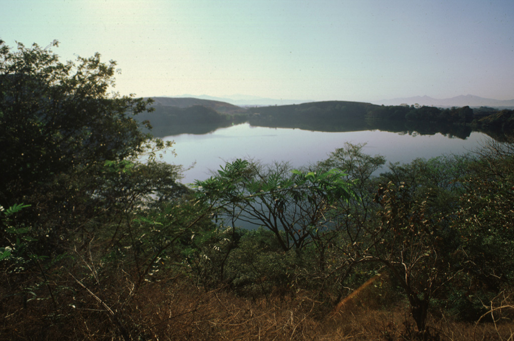 The low SW rim of Aramuaca maar is reflected in the waters of 600-m-wide Laguna de Aramuaca.  The maar was erupted through sediments in a plain north of the Río Grande de San Miguel.  Photo by Giuseppina Kysar, 1999 (Smithsonian Institution).
