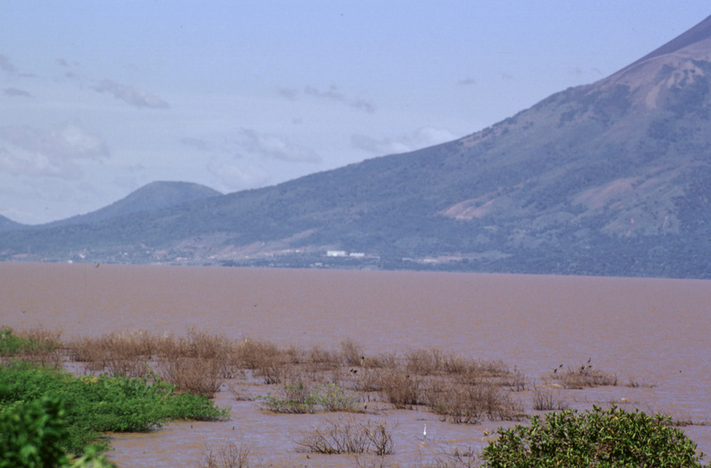 The buildings seen in the center of the photo along the shore of Lake Managua are part of the Patricio Arguello Ryan geothermal plant on the lower southern flank of Momotombo volcano.  At one point the power plant produced 25% of electrical power generation for the country.  In the distance on the left horizon is Cerro Montoso, a peak on the rim of Monte Galán caldera. Photo by Paul Kimberly, 1998 (Smithsonian Institution).