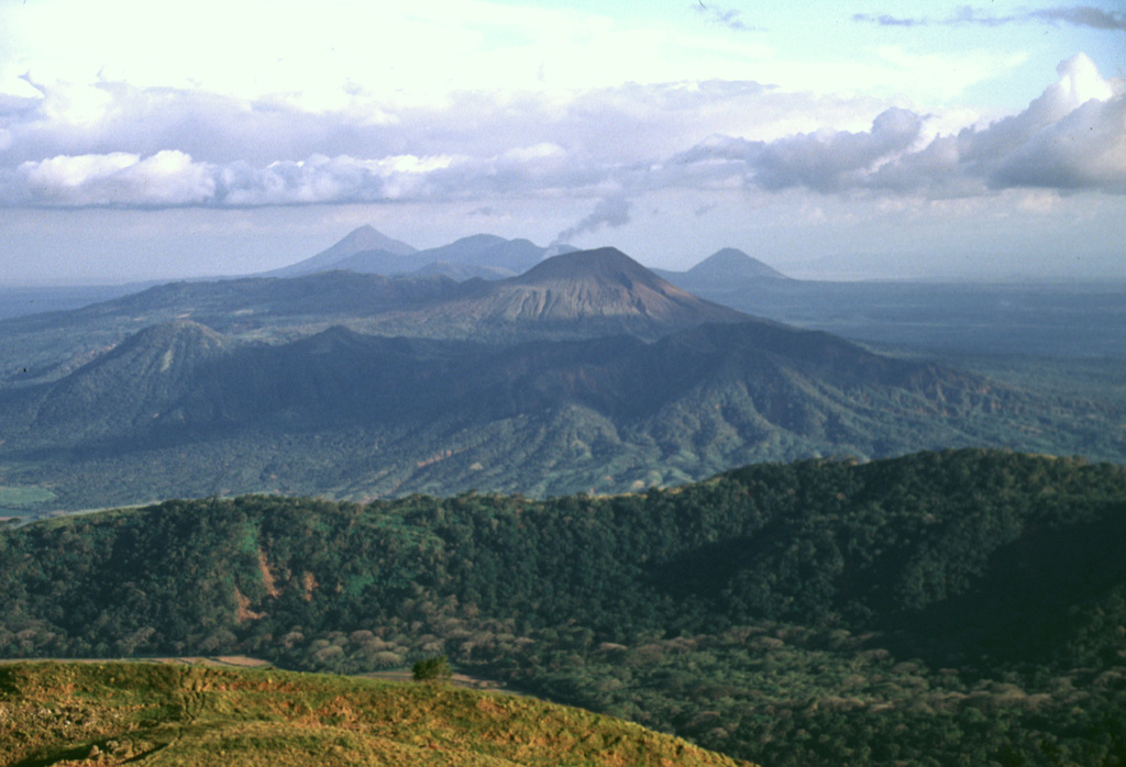 A view from Casita volcano to the SE along the Marrabios Range shows the Telica volcanic complex covering much of the center of the photo.  A thin steam plume rises from the summit of Telica itself (right-center), while the cone of Cerro de Aguero lies at the left-center, with shadows defining older, more dissected parts of the Telica complex.  The forested ridge of La Pelona caldera (part of the San Cristóbal complex) cuts across the lower part of the photo, while Momotombo (left), Las Pilas, and Cerro Asososco (right) lie on the horizon. Photo by Lee Siebert, 1998 (Smithsonian Institution).