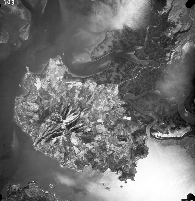 Isla Zacate Grande forms a peninsula bounded by the Gulf of Fonseca at the bottom of the photo and Chismuyo Bay at the left.  Deep erosional valleys descend from the summit of the eroded stratovolcano, which is connected to the Honduras mainland by tidal flats cut by numerous small estuaries seen at the upper right.  More than a half dozen younger satellitic cones, some of which may be Holocene in age, surround the volcano.  The tip of Isla el Tigre lies across the narrow 2-km-wide strait from Zacate Grande. Aerial photo by Instituto Geográfico Nacional El Salvador.