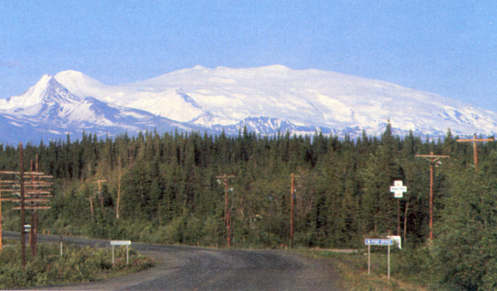 Alaska's Mount Wrangell is one of the most voluminous shield volcanoes in the world and is more than three times the volume of Rainier. It has a diameter of 30 km at 2,000 m elevation and a volume of about 900 km3. Eruption of unusually-low viscosity andesitic lavas at high eruption rates produced long lava flows that contributed to its low-angle morphology. The small snow-covered peak on the left is Mount Zanetti, a flank vent with about the same volume as St. Helens. Wrangell is seen here from Glennallen, 80 km to the west. Photo by Chris Nye (Alaska Division of Geological and Geophysical Surveys).