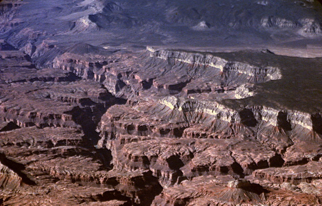 The small dark-colored pyroclastic cone on the right side of the Grand Canyon at the upper left is Vulcan's Throne, part of the Uinkaret volcanic field, which lies on the north rim of the canyon.  Lava flows that originated from the cone can be seen cascading into the Grand Canyon.  These flows formed temporary lava dams in the canyon up to 200 m high.  Light-colored rocks of the Kaibab Limestone form the steep cliffs bounding the mesa at the right. Photo by Lee Siebert, 2000 (Smithsonian Institution).