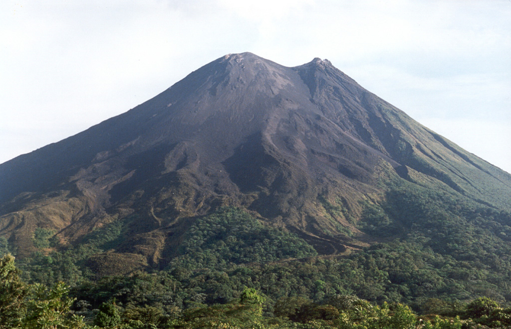 Lava flows from the Arenal eruption that began in 1968 form the surface of the SW flank in this view from the Arenal Volcano Observatory. The active crater (Crater C) is at the summit, while the peak to the right (containing Crater D) is the previous summit. Photo by Jorge Barquero, 1998 (OVSICORI-UNA).