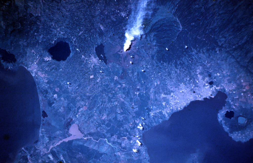 A vigorous steam plume pours from Masaya volcano in this November 9, 1984 Space Shuttle image taken near the end of a two-decade-long eruptive episode.  North lies to the lower right, with Lake Nicaragua at the lower left and Lake Managua at the lower right.  To the left of the plume from Santiago crater is Lake Masaya (ponded against the rim of Masaya caldera) and the circular lake-filled Apoyo caldera.  The two caldera lakes at the lower right are Apoyeque (light blue) and Jiloa (dark-colored), across the bay from the city of Managua. NASA Space Shuttle image STS51A-32-64, 1984 (http://eol.jsc.nasa.gov/).