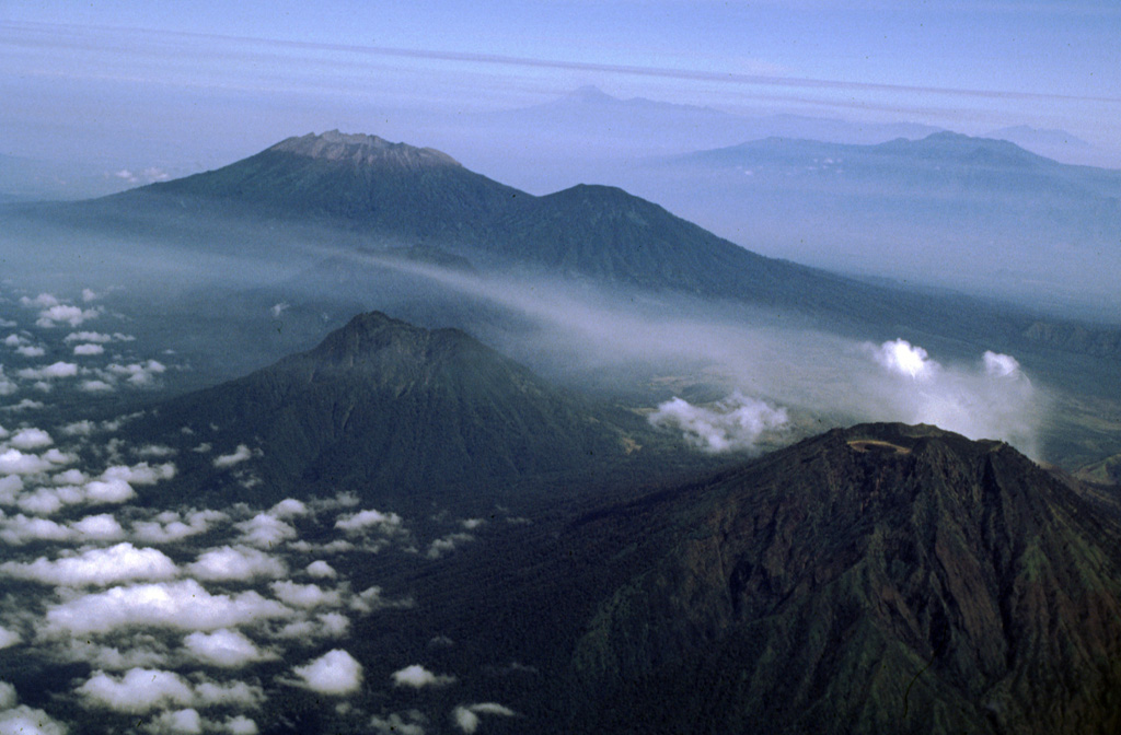 Raung volcano, with its unvegetated summit caldera and Suket peak to the NE, is at the upper left in this aerial view from the eastern tip of Java. In the foreground are Gunung Rante (left-center) and Gunung Merapi (lower right), constructed near the margin of the Ijen caldera complex. The Semeru-Tengger caldera complex is on the far right-center horizon, and the Iyang-Argapura complex is on the upper right. Photo by Lee Siebert, 2000 (Smithsonian Institution).