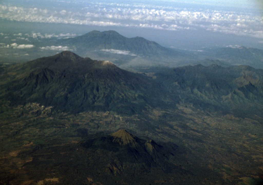 Three young volcanoes in eastern Java are seen in this aerial view from the NE. The Arjuno-Welirang massif lies at the left-center, with Gunung Arjuno forming the high point of the complex and light-colored Gunung Welirang to the NW (right). In the background is the Kawi-Butak massif, with Gunung Butak forming the high point and Gunung Kawi to its right. The smaller conical peak of Penanggungan rises above lowlands in the foreground. Photo by Lee Siebert, 2000 (Smithsonian Institution).