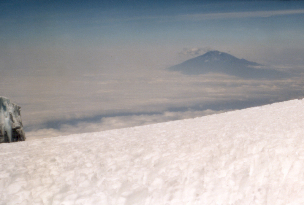 Meru volcano (upper right), Africa's fourth highest mountain, is seen from the ice-covered summit plateau of neighboring Kilimanjaro volcano. The volcano is cut by a 5-km-wide breached caldera on the E side that formed about 7,800 years ago when the summit collapsed. A massive debris avalanche and lahar traveled to the east as far as the western flank of Kilimanjaro. Photo by Tom Jorstad, 1991 (Smithsonian Institution).