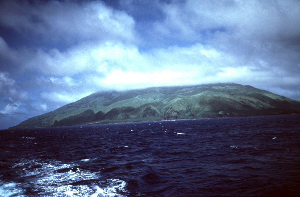 Agrigan is the highest of the Marianas arc volcanoes, seen here from the south. The island is 8 km long and its summit is the top of a large 4-km-high submarine volcano. The summit caldera is 1 x 2 km wide and 500 m deep, and the vegetated flanks consist almost entirely of pyroclastic deposits that are more than 100 m thick on the SW flank. Photo by Dick Moore, 1990 (U.S. Geological Survey).