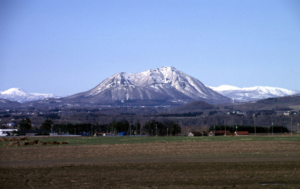Snow-covered Shiribetsu volcano is seen in a winter view rising to the NNE above farmlands near the west side of Lake Toya.  Shiribetsu, located immediately SE of Yotei volcano, is a small, 1107-m-high stratovolcano that contains a 1.5-km-wide crater breached widely to the west.  It was created by a massive debris avalanche that removed the summit, swept more than 7 km to the west, and formed a hummocky deposit at the SE foot of Yotei volcano, out of view to the left.   Copyrighted photo by Shun Nakano (Japanese Quaternary Volcanoes database, RIODB, http://riodb02.ibase.aist.go.jp/strata/VOL_JP/EN/index.htm and Geol Surv Japan, AIST, http://www.gsj.jp/).