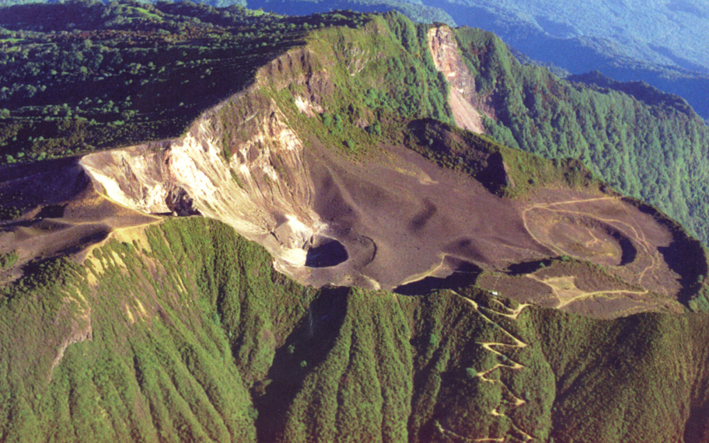 This photo shows the large scarp area that opens towards the NE (right) at the summit of Turrialba, the easternmost Holocene volcano in Costa Rica. The upper part of the scarp is partially filled by a smaller edifice with a roughly 1.3-km-wide crater, containing three smaller craters that erupted during the 18th-19th centuries. The walls of the two SW-most craters expose light-colored, hydrothermally altered rocks. Geothermal activity continues at these craters. Photo by Federico Chavarria Kopper, 1999.