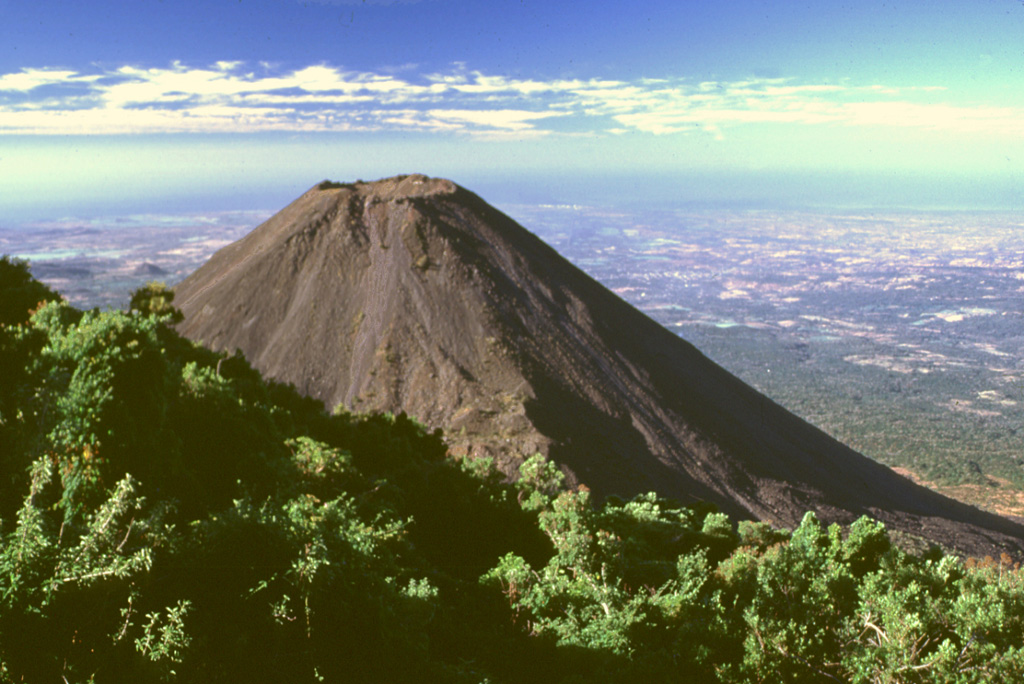 The flanks of Izalco volcano contrast with the vegetated Cerro Verde in the foreground. Izalco rises about 300 m above the saddle separating it from Cerro Verde. This view shows the Pacific Ocean 40 km to the south with much of the area between underlain by deposits associated with a late-Pleistocene Santa Ana debris avalanche. Photo by Lee Siebert, 2002 (Smithsonian Institution).