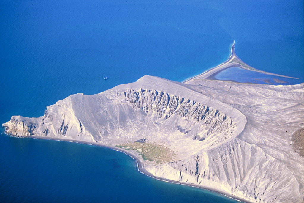The Plaza de Toros tuff ring on the SE side of Isla San Luis is seen here from the east in 2000. Remnants of dacite lava flows are visible in the upper walls of the crater. Only a third of the tuff ring is still standing; the rest has subsided along normal faults or was eroded by wave action. Longshore currents have redistributed volcanic deposits to produce the tombolo to the upper right that forms the SW tip of the island and is 2 km long at low tide. Photo by Keith Sutter, 2000.