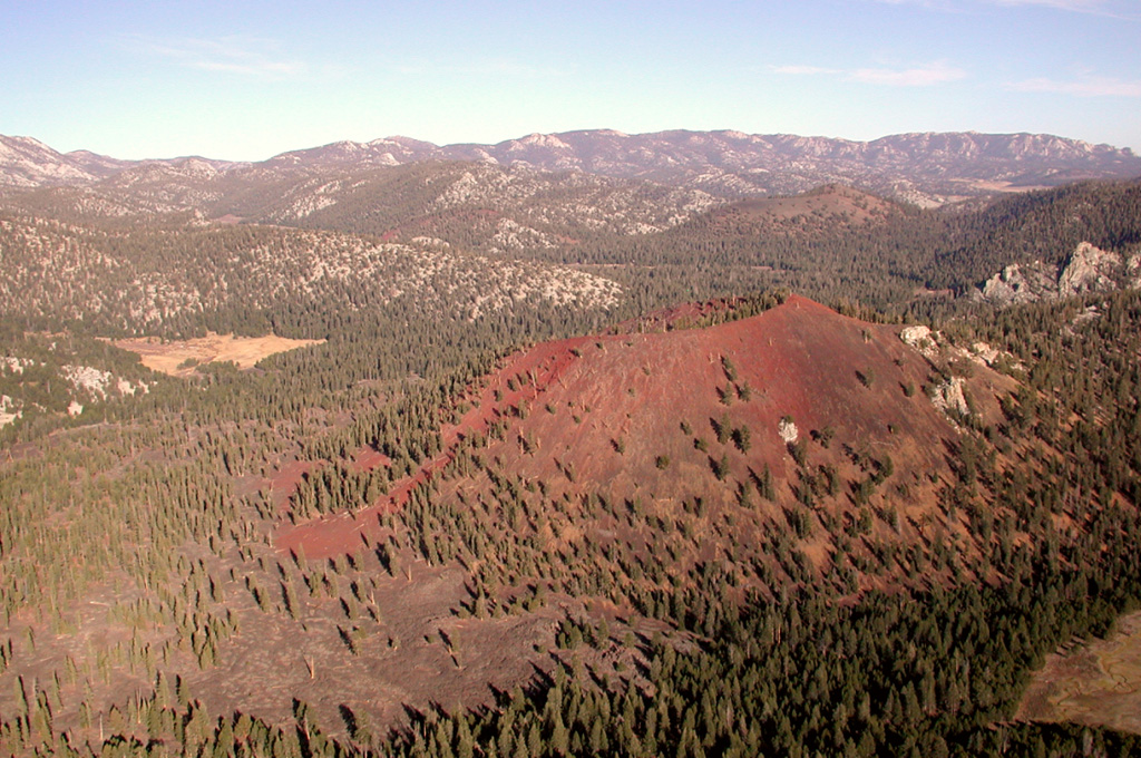 Reddish oxidized scoria mantles the slopes of Groundhog cinder cone, the youngest of Golden Trout Creek volcanic field.  The cone is seen here from the west, with Tunnel cone (left center) and South Fork cone (beyond the right-hand rim of Groundhog) behind it.  The light-colored area at the left center is Groundhog Meadow.  Basaltic lava flows from Groundhog cone visible at the lower left extended 6 km down Golden Trout Creek. Photo by Rick Howard, 2002 (courtesy of Del Hubbs, U S Forest Service).