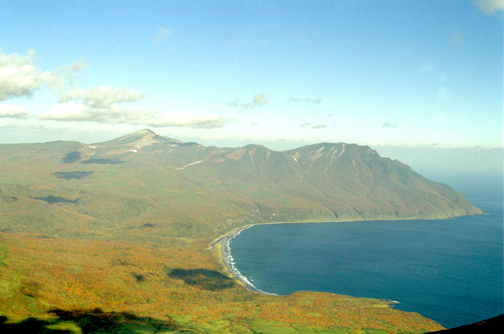 Rakkibetsudake volcano, forming the peninsula to the right, is seen from the summit of Srednii volcano of the Moyorodake volcanic complex on Iturup island. It grew during the Holocene within a glacial valley 3 km E of the eroded Pleistocene Kamui volcano, the higher peak on the left horizon. The summit contains a 1.5-km-wide crater that opens to the east. Photo by Alexander Rybin, 1995 (Institute of Marine Geology and Geophysics, Yuzhno-Sakhalin).