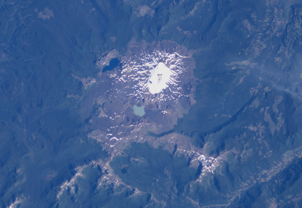 Quetrupillan stratovolcano is seen in this NASA International Space Station image with north to the upper right.  The volcano was constructed within a large 7 x 10 km wide caldera.  The 2360-m-high Quetrupillan volcano has produced more silicic lavas than its more prominent neighbors Villarrica and Lanín.  Clusters of monogenetic vents, including lava domes and pyroclastic cones, are found on the southern side of the volcano. NASA International Space Station image ISS006-E-40424, 2003 (http://eol.jsc.nasa.gov/).