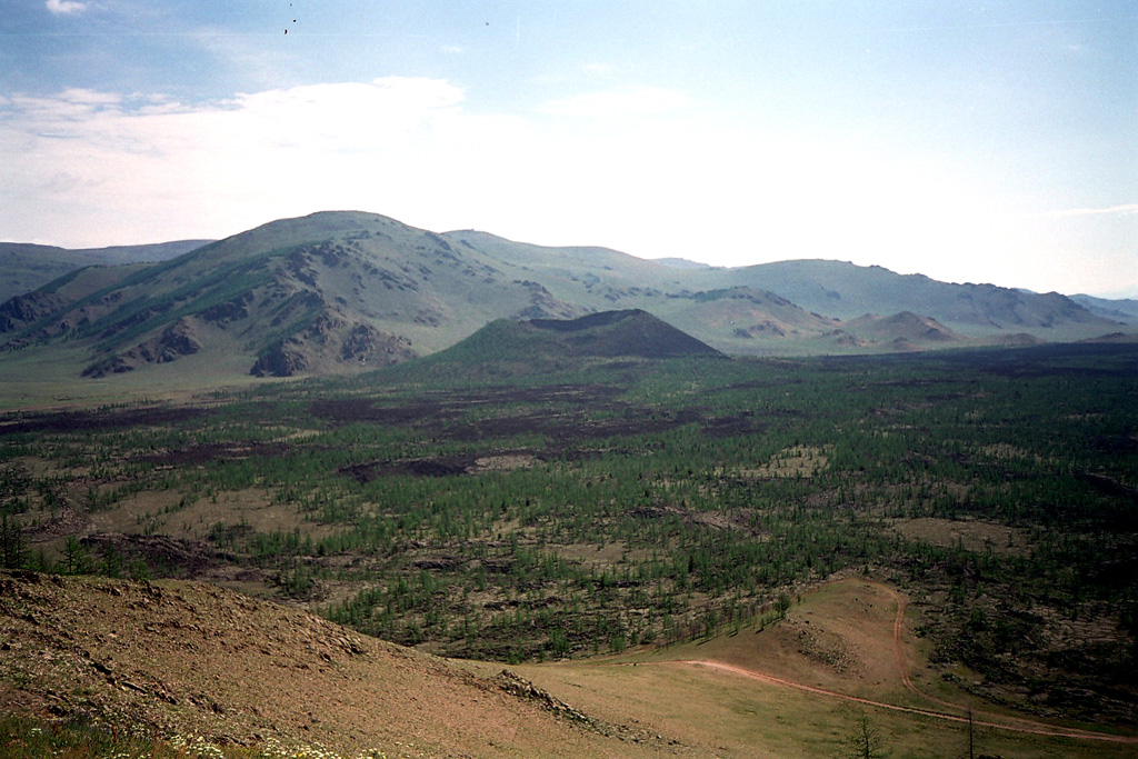 The sparsely vegetated lava flow filling this valley originated from Horgo scoria cone (center). The cone is part of the Taryatu-Chulutu volcanic field in north-central Mongolia about 250 km W of Ulaanbaatar. The volcanic field contains six Holocene scoria cones along the Sumein and Gichgeniyn river valleys at the western end of the volcanic field.  Photo by Piotr Olszewski, 2004.