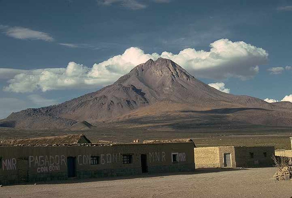 Symmetrical Tata Sabaya stratovolcano towers to the north above the village of Pagador in the Altiplano of Bolivia.  Thick dacitic lava flows at the left partially cover a scarp from a major collapse of the edifice that produced a large debris avalanche which swept into the Salar de Coipasa, covering an area of more than 300 km2 south of the volcano.  The morphology of the volcano has been subsequently modified by dome emplacement (left and right) and hot avalanches. Photo by Jon Davidson (University of Durham).