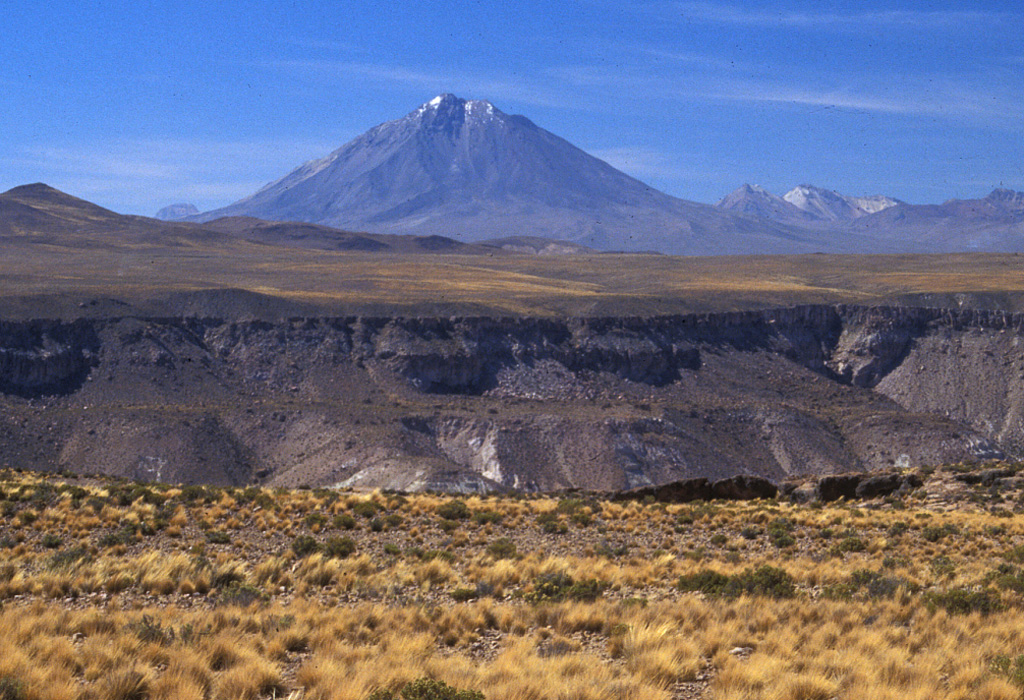 Tacora, the northernmost volcano of Chile, rises to the NW above the steep-walled Allane valley.  The 5980-m-high Tacora lies near the border with Perú and is a twin volcano with Chupiquina, hidden behind Tacora in this view.  Although there have been uncertain reports of historical eruptions, and solfataric and fumarolic activity has been reported on the east side, Holocene eruptions have not been documented.  The Arica to La Paz railway transects the plateau on the northern side of the Allane valley. Photo by Lee Siebert, 2004 (Smithsonian Institution).