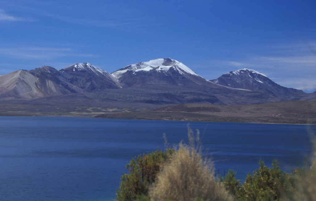 Three N-S-trending volcanoes of the Quimsachata chain rise along the Chile-Bolivia border above the SW shore of Laguna Chungará.  From left to right, they are 5730-m-high Volcán Humarata, 6052-m-high Volcán Acotango, and 5990-m-high Cerro Capurata volcanoes.  No historical eruptions are known from the chain, but Acotango volcano has a youthful morphology with lava flows of inferred late-Pleistocene age.  Its broad summit crater is open to the north and is the source of a large andesitic-dacitic lava flow.   Photo by Lee Siebert, 2004 (Smithsonian Institution).
