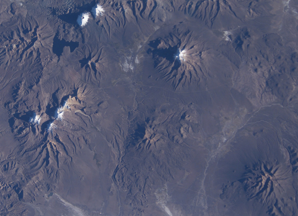 Snow capped volcanoes dot this NASA International Space Station image (with north to the upper right) taken along the Chile-Bolivia border.  The snow-capped peak at the far left-center is Guallatiri volcano, and to its right are the three peaks of Nevados Quimsachata, which includes Acotango volcano.  The two peaks at the upper left are Pomerape and Parinacota, with Laguna Chungara below.  Nevado del Sajama in Bolivia lies at the upper right-center.  At the lower right is the snow-free volcano of Macizo de Larancagua. NASA International Space Station image ISS009-E-6848, 2004 (http://eol.jsc.nasa.gov/).