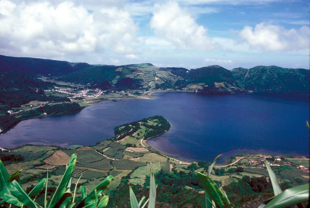 A small peninsula extends into Lagoa Azul ("Blue Lake"), one of two main lakes partially filling the floor of the summit caldera on Sete Cidades volcano at the western end of Sao Miguel Island. The 5-km-wide caldera was formed in three major eruptions at about 36,000, 29,000 and 16,000 years ago, and at least 17 eruptions have occurred here in the last 5,000 years. This view looks to the northwest from the rim of a post-caldera cone containing Lagoa Santiago. Two other post-caldera cones, Caldeira do Alferes and Seara, lie across the lake, behind and to the right of the town of Sete Cidades. Photo by R.V. Fisher, 1980 (University of California Santa Barbara).