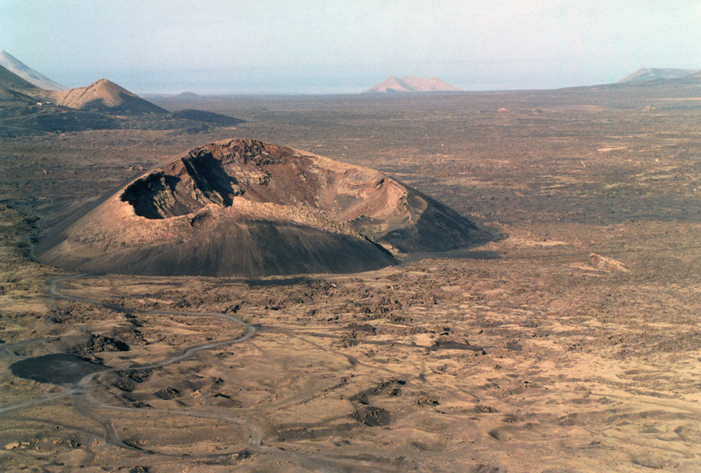 The Caldera de los Cuervos (left center) was formed during the initial stage of the eruption during 1730 to 1736. Eruptions from a 13-15 km long NE-SW trending fissure formed more than 30 cones and produced voluminous lava flows that covered about 250 km2, reaching the western coast. A third of the farmland and numerous villages were buried in ash during this six-year long eruption.  Photo by Raphaël Paris, 2001 (CNRS, Clermont-Ferrand).