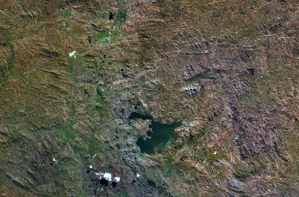 The Itasy volcanic field in central Madagascar lies W of Lake Itasy (lower center) and consists of a N-S-trending chain of scoria cones, lava domes, and maars. Several small dark-colored, lake-filled maars can be seen in the NASA Landsat image (N to the top), one of which lies just above the NW arm of Lake Itasy. Early eruptions producing trachytic lava domes and basanitic lava flows were followed by the effusion of trachytic lava flows and recent Vulcanian eruptions. Mild seismicity and hot spring activity continue at Itasy. NASA Landsat 7 image (worldwind.arc.nasa.gov)
