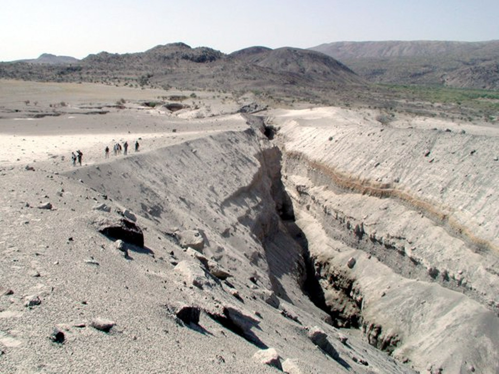 The slopes of Dabbahu volcano in the background are part of a large volcanic massif consisting of obsidian flows, lava domes, cones, and basaltic lava flows constructed on a shield volcano. This view from the N with people for scale shows Da'Ure, a 500-m-long fissure vent formed during the first historical eruption in September 2005. A small dome was formed during the eruption. The central part of the volcano lies farther to the right off the margin of the photo. Photo by Anthony Philpotts, 2005 (University of Connecticut).