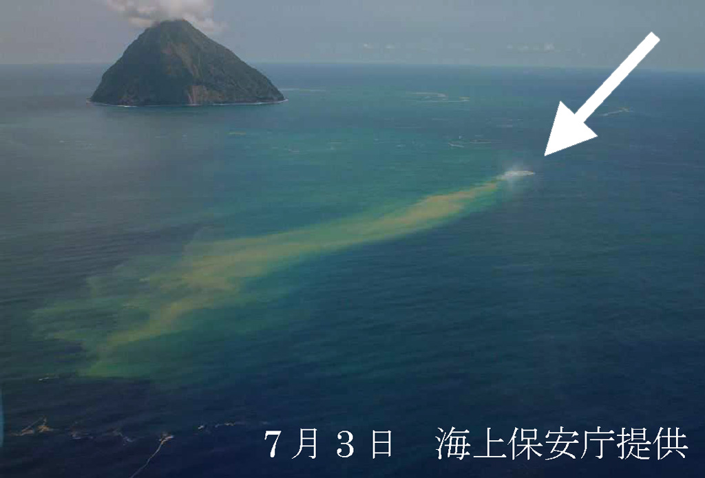 Fukutoku-Oka-no-ba on 3 July 2005 from the NE shows a plume of debris and discoloration extending from the arrow. On the previous day a white plume was observed, which later reached about 1 km above the ocean surface. Numerous large and steaming floating blocks were seen at mid-day on 3 July. The island in the background is Shin-Iwojima. Photo courtesy of Japan Maritime Security and Safety Agency, 2005.