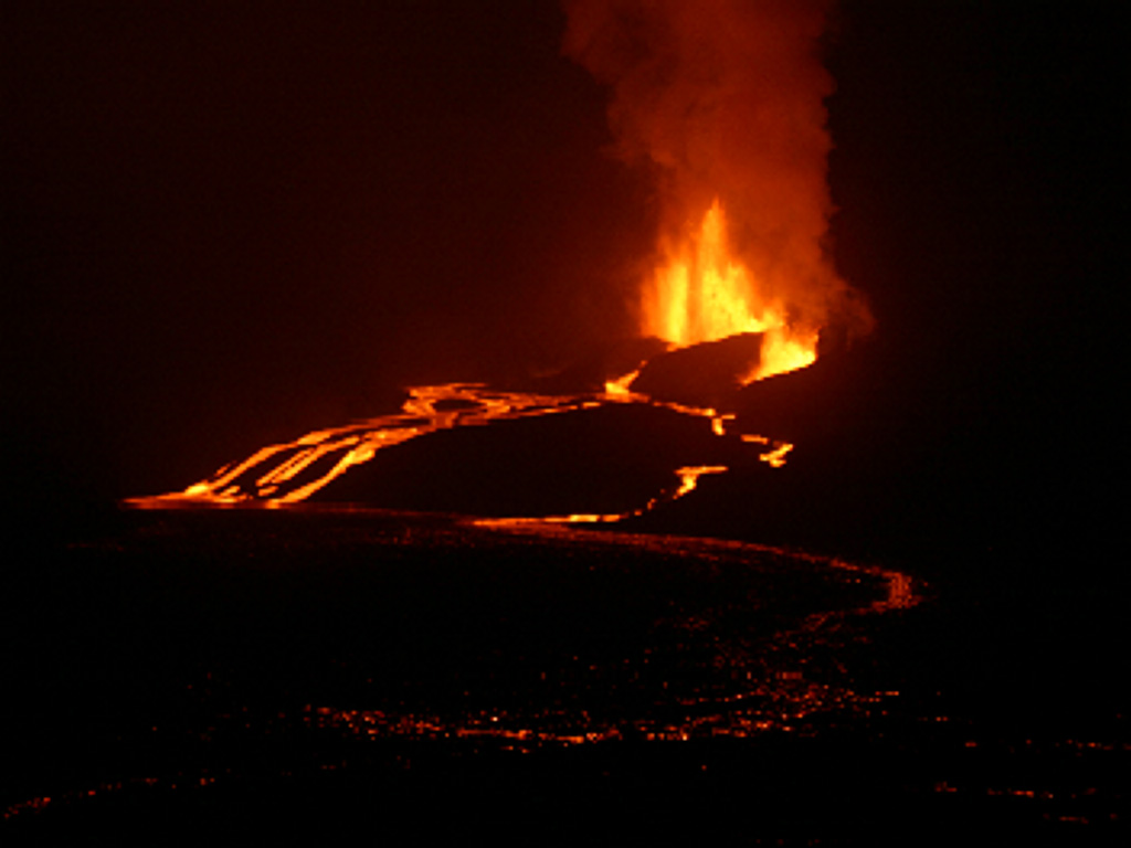 Lava fountaining of the Sierra Negra eruption is viewed from the east caldera rim on the night of October 24, the 3rd day of the eruption.  Vigorous lava fountains rise from several locations along the fissure vent, feeding several anastomosing lava flows that poured into the caldera.  The scattered glow in the foreground was due to ponded lava covering the caldera's eastern floor. Photo by Gregg Estes, 2005.