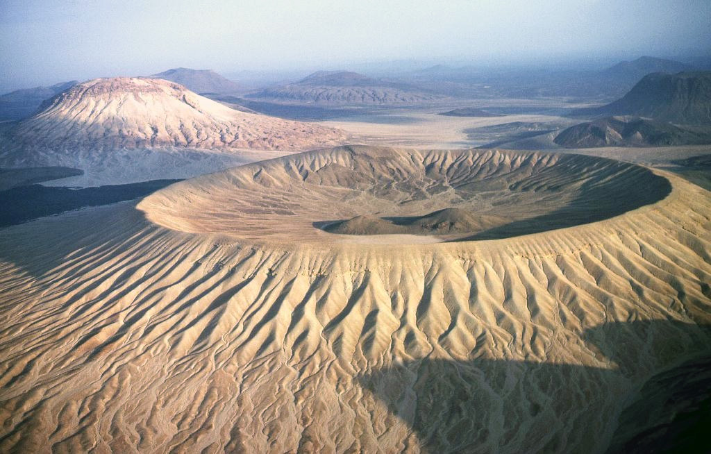 Light-colored lapilli deposits mantle the Jabal Bayda ("White Mountain") tuff cone; a lava dome is visible within the crater. Jabal Bayda and the Jabal Abyad lava dome (upper left) are part of the 14,000 km2 Harrat Khaybar volcanic field, located N of the city of Madinah (Medina). A 100-km-long N-S linear vent system in Harrat Khaybar contains lava domes, tuff rings, the Jabal Qidr stratovolcano, and numerous small basaltic cones. Copyrighted photo by Michael Fenton, USGS (courtesy Earth Science World Image Bank http://www.earthscienceworld.org/images)