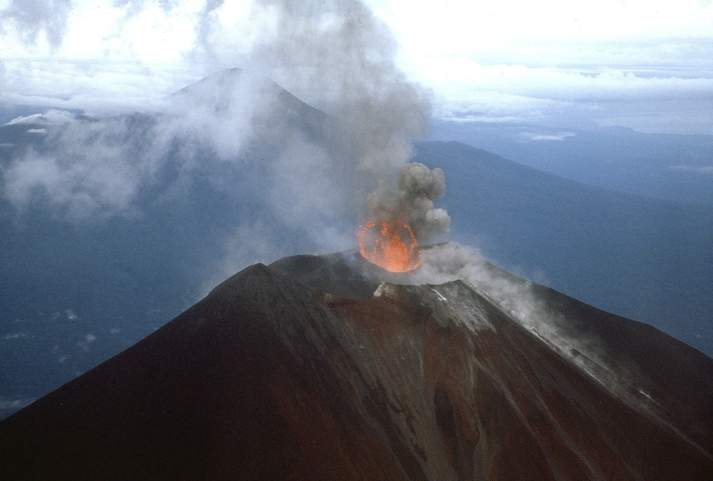 Photograph of Ulawun taken from a helicopter on 25 November 1985. This view from the NE shows the ejection of lava into the air above the vent during Strombolian activity. The other large stratovolcano in the background is Bamus.  Photo by James Mori, Disaster Prevention Research Institute, Kyoto University.