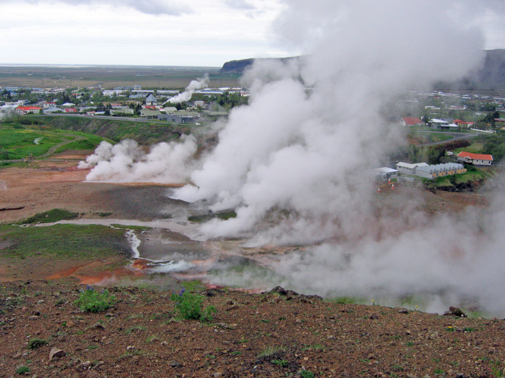 Steam plumes, newly formed after a May 2008 earthquake, rise from the Reykir ("smokes" in Icelandic) geothermal area, with the town of Hveragerdi in the background. The Hveragerdi geothermal field lies within the small Pleistocene Grensdalur volcanic system, the oldest of three volcanic systems in the Hengill area. The geothermal field include fumaroles, hot springs and pools, mud pots, and geysers, and provides heat to the town of Hveragerdi. Photo coutesy of the University of Iceland Hvergerdi Research Station, 2008.