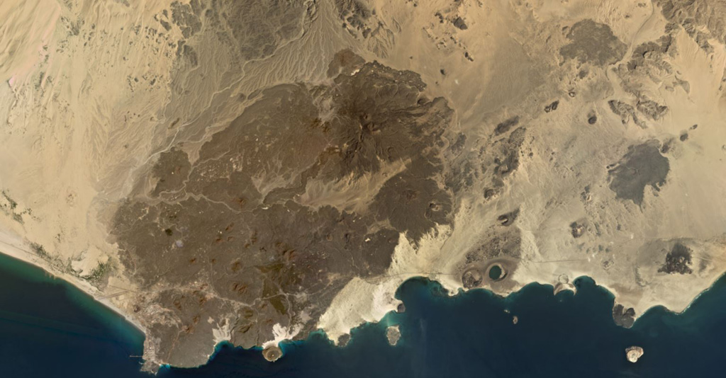 The 500 km2 Balhaf-Bir Ali Volcanic Field in south Yemen is shown in this February 2020 Planet Labs satellite image monthly mosaic (N is at the top; this image is approximately 45 km across). The field largely comprises lava flows and spatter and scoria cones, tuff rings, and the At-Tabâb maar with a crater lake along the shoreline. The Balhaf cone is the darker area to the S with the cross-roads just below it, and the darker area in the northern part of the field is the Jabal Ba Masha’ib. Satellite image courtesy of Planet Labs Inc., 2020 (https://www.planet.com/).
