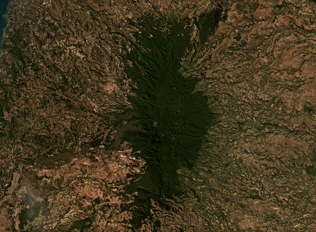 The Ambre-Bobaomby volcanic field forms the northernmost region of Madagascar, shown in this July 2019 Planet Labs satellite image monthly mosaic (N is at the top; this image is approximately 47 km across). The edifice shown here is the Massif d’Ambre, and the Bobaomby field continues to the north. The Massif d’Ambre contains lava flows, spatter cones, tuff rings, pyroclastic flow deposits, and tephra, with some craters visible down the apex of the N-S trending edifice. Satellite image courtesy of Planet Labs Inc., 2019 (https://www.planet.com/).