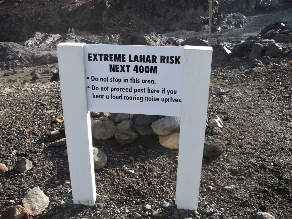 This “extreme lahar risk” sign is on the northern side of the Whangaehu valley on the E flank of Ruapehu with the September 2007 lahar in the background, the second lahar down this path that year. The bridge visible beyond the sign was damaged by the lahars. Photo by Janine Krippner, 2007.
