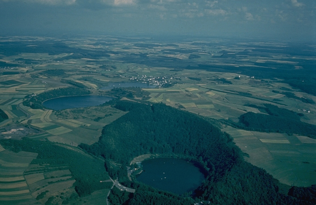 An aerial view from the NW provides an overview of three lake-filled maars, the Gemunden maar in the foreground, and the Weinfeld and Schalkenmehren maars at the left center.  Explosive eruptions through nonvolcanic bedrock during the late Pleistocene formed craters with low rims of volcanic ejecta.  The West Eifel volcanic field of western Germany contains about 240 scoria cones and maars. Copyrighted photo by Katia and Maurice Krafft.