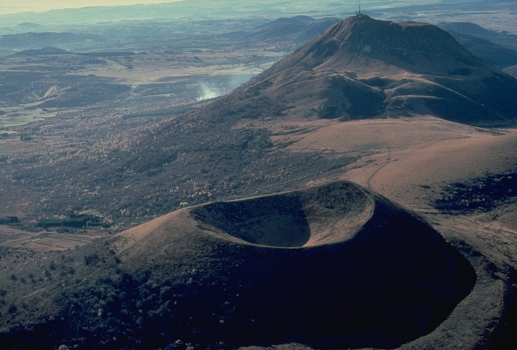 The Puy de Pariou cinder cone in the foreground and the Puy de Dôme lava dome in the background are part of a long N-S chain of volcanoes forming the Chaîne des Puy volcanic field in west-central France.   The Puy de Pariou was formed about 8200 years ago inside a tuff ring from an earlier eruption whose rim can be seen at the lower right. Copyrighted photo by Katia and Maurice Krafft, 1978.
